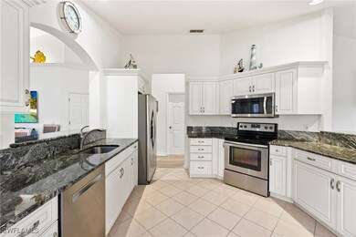 Kitchen featuring stainless steel appliances, dark stone countertops, white cabinetry, light tile patterned flooring, and a high ceiling