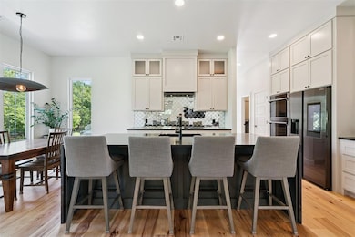 Kitchen with a center island with sink, backsplash, glass insert cabinets, stainless steel appliances, and light wood-style flooring