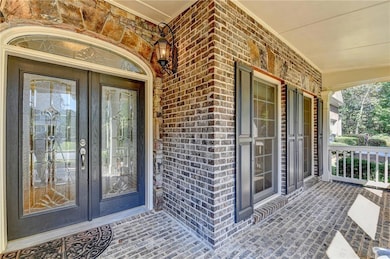 Doorway to property with covered porch, brick siding, and french doors