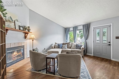 Living room with a textured ceiling, lofted ceiling, a tiled fireplace, and wood finished floors