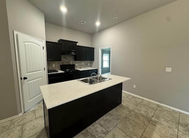 Kitchen featuring dark cabinets, tasteful backsplash, a kitchen island with sink, black range, and under cabinet range hood