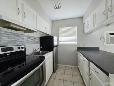 Kitchen with stainless steel appliances, tasteful backsplash, dark countertops, white cabinetry, and under cabinet range hood