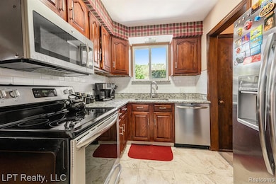 Kitchen featuring appliances with stainless steel finishes, decorative backsplash, and light stone counters