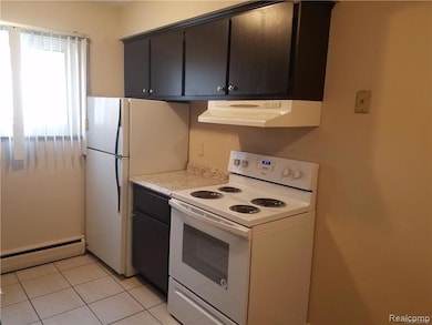 Kitchen with white appliances, baseboard heating, range hood, light countertops, and light tile patterned floors