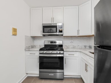 Kitchen featuring tile patterned flooring, tasteful backsplash, light stone counters, white cabinetry, and stainless steel appliances
