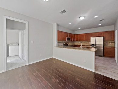 Kitchen featuring brown cabinetry, appliances with stainless steel finishes, a peninsula, light stone countertops, and washer / dryer