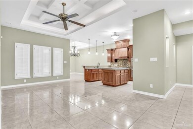 Kitchen featuring a tray ceiling, tasteful backsplash, a center island with sink, pendant lighting, and ceiling fan with notable chandelier