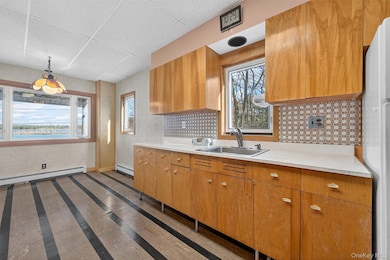 Kitchen with wallpapered walls, light countertops, a drop ceiling, brown cabinets, and freestanding refrigerator