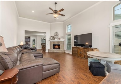 Living room featuring ornamental molding, wood finished floors, ceiling fan, a towering ceiling, and a fireplace