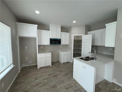 Kitchen featuring a sink, stainless steel microwave, a peninsula, white cabinets, and recessed lighting