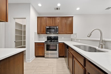 Kitchen with appliances with stainless steel finishes, brown cabinets, recessed lighting, backsplash, and light stone countertops