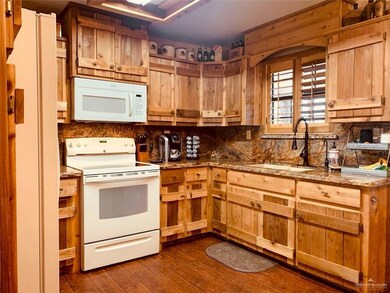 Kitchen with white appliances, dark wood-style flooring, tasteful backsplash, and light stone countertops