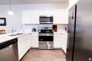 Kitchen featuring stainless steel appliances, light wood-style flooring, light countertops, white cabinetry, and pendant lighting