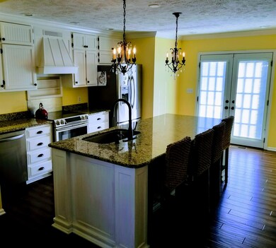 The open kitchen features white cabinetry, granite counter tops & island.  