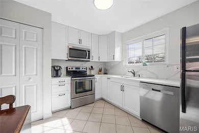 Kitchen with stainless steel appliances, light tile patterned flooring, decorative backsplash, and white cabinets