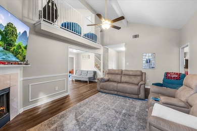 Living room featuring a tiled fireplace, high vaulted ceiling, wood finished floors, beamed ceiling, and ceiling fan