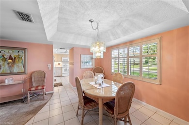 Dining room featuring a textured ceiling, light tile patterned flooring, a tray ceiling, and a chandelier
