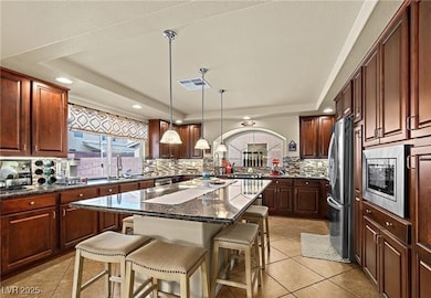 Kitchen featuring a raised ceiling, a breakfast bar, dark stone counters, light tile patterned flooring, and stainless steel appliances
