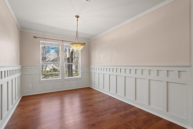 Unfurnished dining area featuring a wainscoted wall, ornamental molding, dark wood finished floors, a decorative wall, and a chandelier