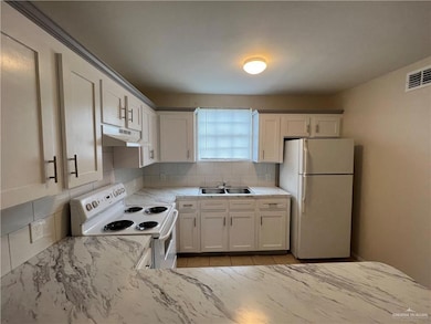 Kitchen featuring white appliances, under cabinet range hood, backsplash, a sink, and light stone counters