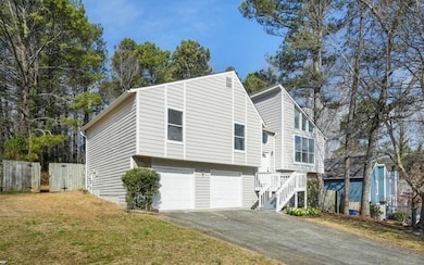 View of property exterior featuring driveway, an attached garage, a yard, and fence