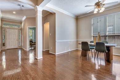 Dining space featuring a textured ceiling, crown molding, hardwood / wood-style floors, arched walkways, and ornate columns
