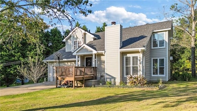 Back of house featuring roof with shingles, a lawn, concrete driveway, a chimney, and a deck