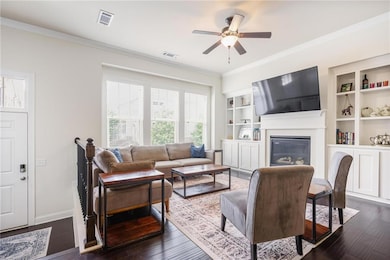 Living room featuring a ceiling fan, a glass covered fireplace, ornamental molding, dark wood-style floors, and built in features