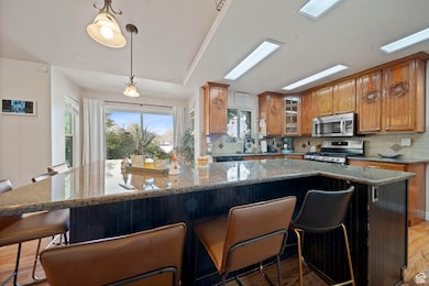 Kitchen with a kitchen bar, dark stone countertops, glass insert cabinets, backsplash, and stainless steel appliances