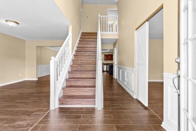 Stairway featuring wood finish floors, a high ceiling, a decorative wall, a wainscoted wall, and a textured ceiling