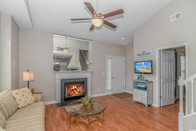 Living room with a glass covered fireplace, wood finished floors, ceiling fan, baseboards, and high vaulted ceiling