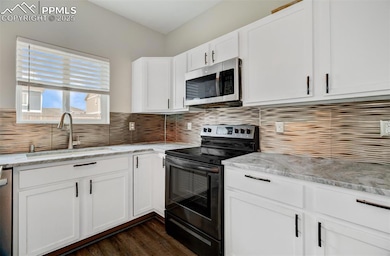Kitchen featuring stainless steel appliances, decorative backsplash, white cabinets, dark wood-style floors, and light stone counters