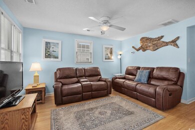 Living room with a textured ceiling, light wood-style floors, a ceiling fan, and healthy amount of natural light