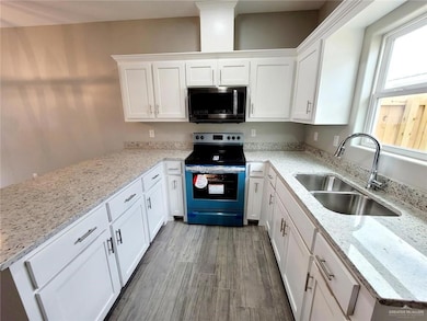 Kitchen with white cabinets, a sink, wood finished floors, light stone countertops, and range with electric stovetop
