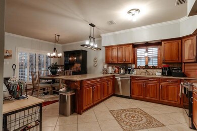 Kitchen with appliances with stainless steel finishes, backsplash, brown cabinetry, ornamental molding, and light tile patterned floors