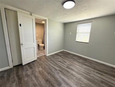 Unfurnished bedroom featuring a textured ceiling, dark wood-style floors, baseboards, and connected bathroom