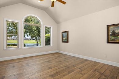 Primary bedroom featuring vaulted ceiling, wood-type flooring, and ceiling fan, overlooking backyard, pool, pond and golf course
