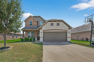 This photo shows a charming two-story brick and stone house with a double garage, a well-maintained lawn, and a basketball hoop. The home features a welcoming front porch and is located in a suburban neighborhood.
