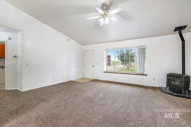 Unfurnished living room with a wood stove, vaulted ceiling, carpet, and ceiling fan