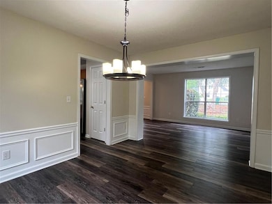 Unfurnished dining area featuring a chandelier, dark wood-style flooring, wainscoting, and a decorative wall