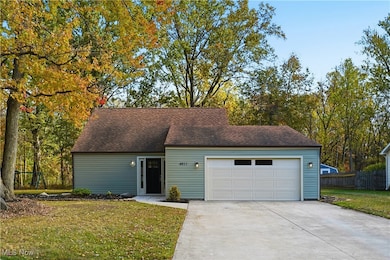 View of front of house with concrete driveway, a front yard, a garage, and view of wooded area