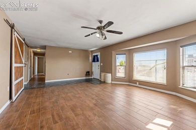 Unfurnished living room with a barn door, a ceiling fan, wood finished floors, and baseboards