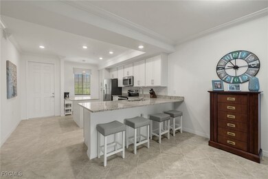 Kitchen with a breakfast bar, a peninsula, light stone countertops, white cabinetry, and crown molding