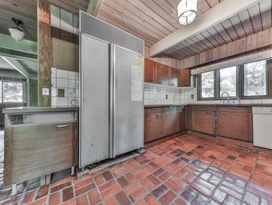 Kitchen featuring paneled built in refrigerator, plenty of natural light, brick flooring, dishwasher, and a wood ceiling with exposed beams