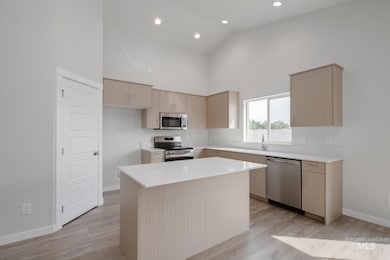 Kitchen featuring light brown cabinetry, high vaulted ceiling, stainless steel appliances, modern cabinets, and a center island