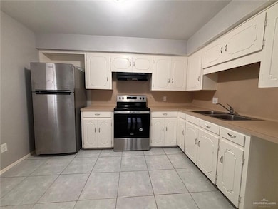 Kitchen featuring light tile patterned floors, a sink, under cabinet range hood, white cabinetry, and stainless steel appliances