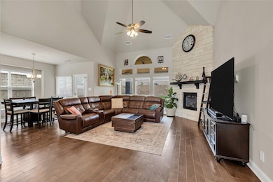 Living room featuring high vaulted ceiling, a stone fireplace, dark wood-style floors, and a ceiling fan