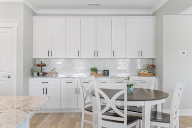 Kitchen featuring white cabinetry, light stone countertops, backsplash, and ornamental molding
