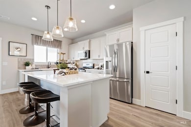 Kitchen with appliances with stainless steel finishes, white cabinets, pendant lighting, a breakfast bar, and decorative backsplash