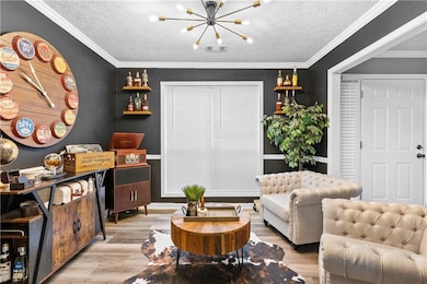 Living room featuring a chandelier, light wood-type flooring, a textured ceiling, and crown molding
